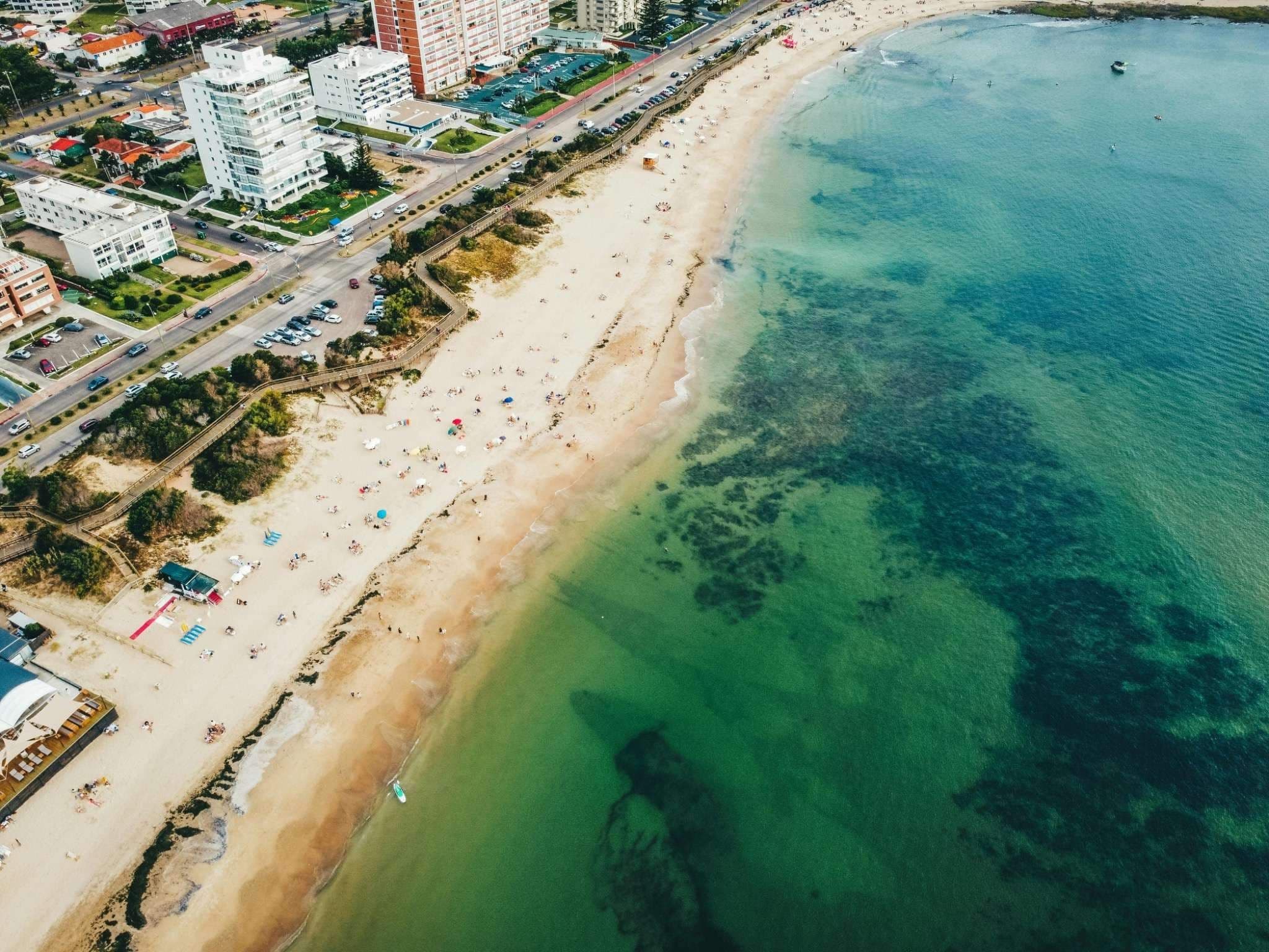 Aerial view of Maldonado coastline with beach, residential buildings, and turquoise water showing urban growth in Uruguay